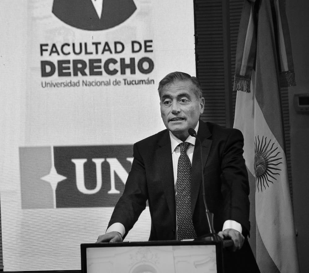 Madkur, en blanco y negro, hablando en el atril de la Facultad de Derecho junto a la bandera argentina.